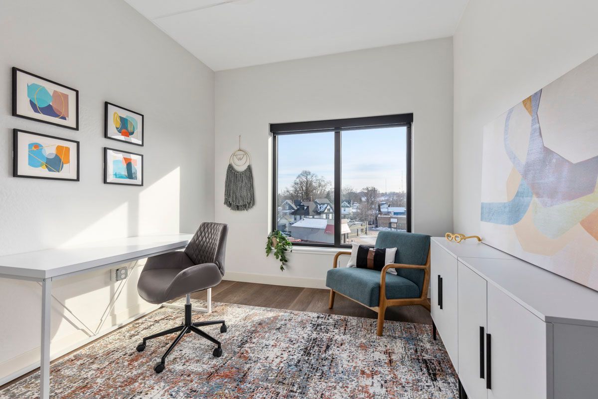 Bright home office with desk, swivel chair, window seat, and colorful wall art.