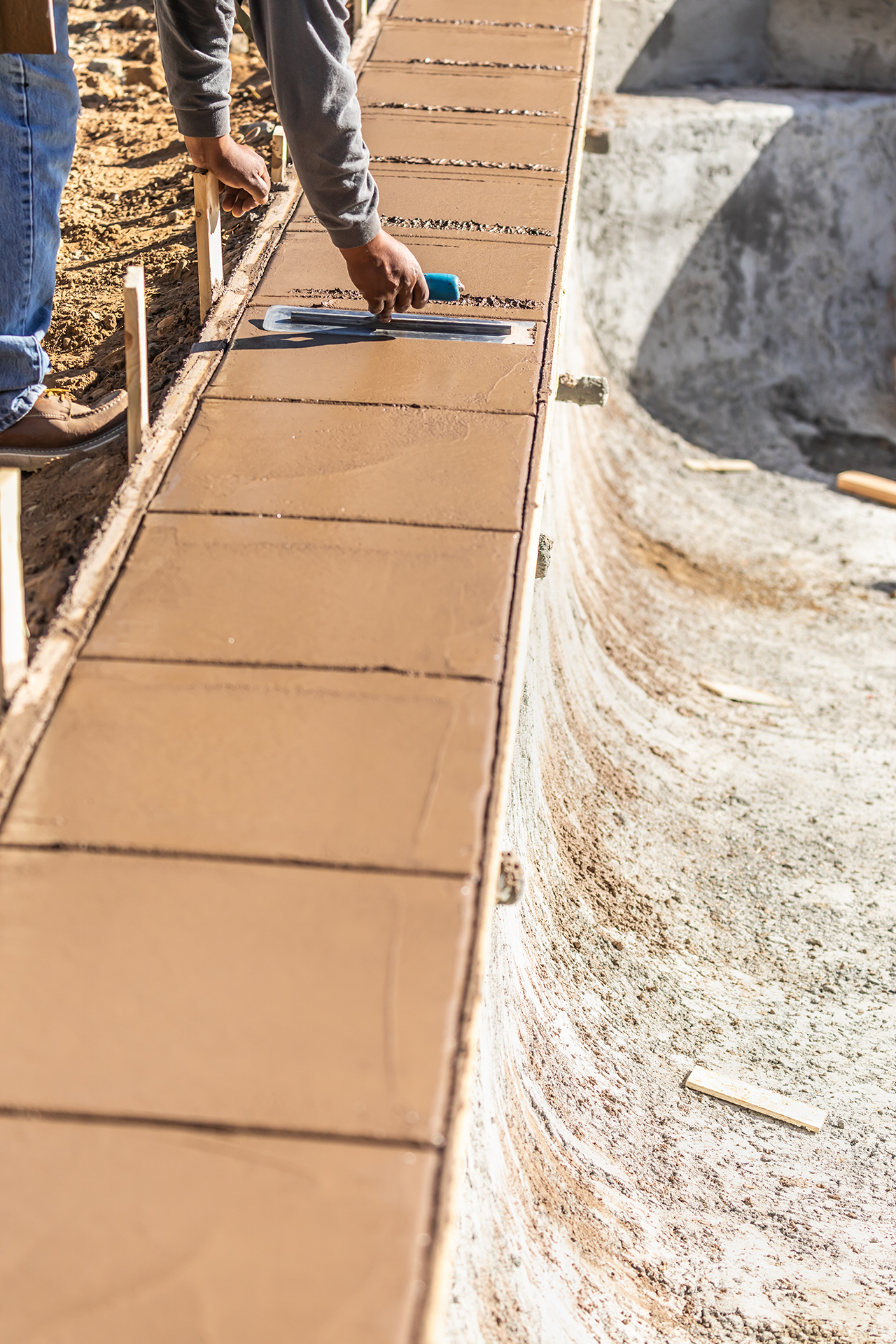 A man is laying concrete on a sidewalk next to a pool.