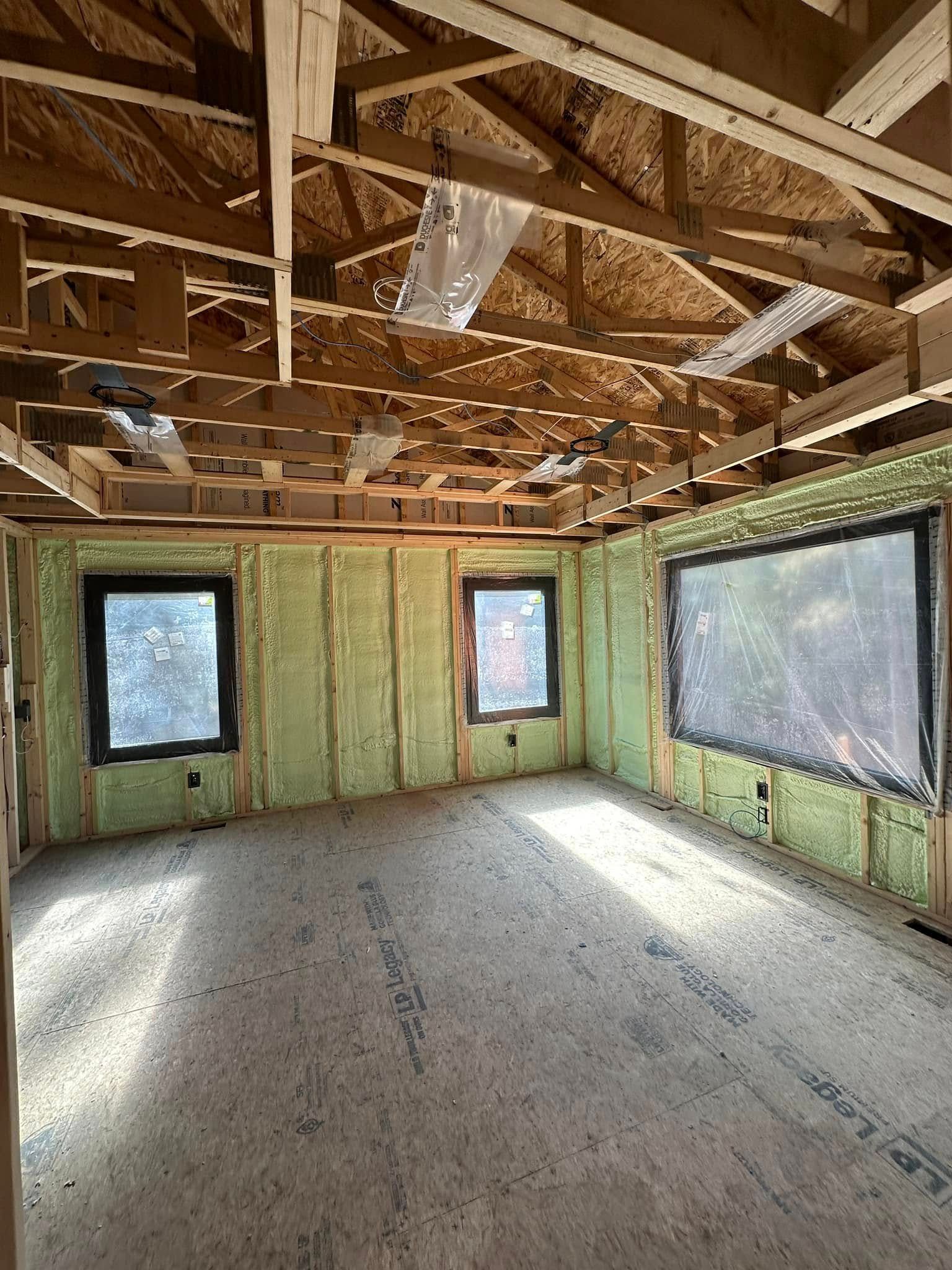 An empty room with green insulation and windows under construction.