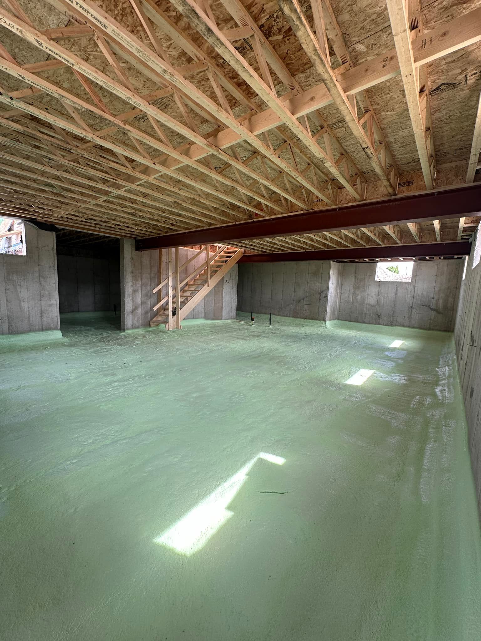 A basement under construction with a green floor and wooden beams.