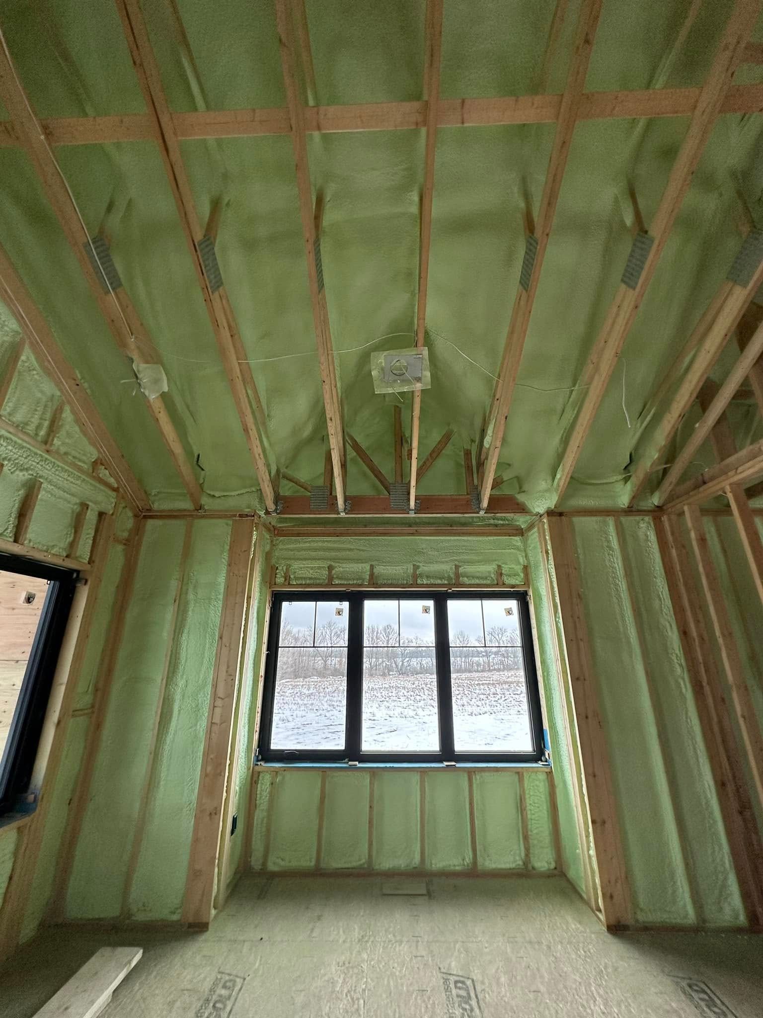 A room with green insulation and a window in a house under construction.