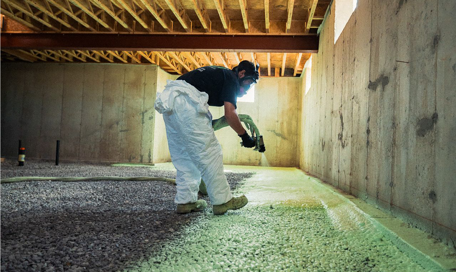 A man is spraying foam on the floor of a basement.