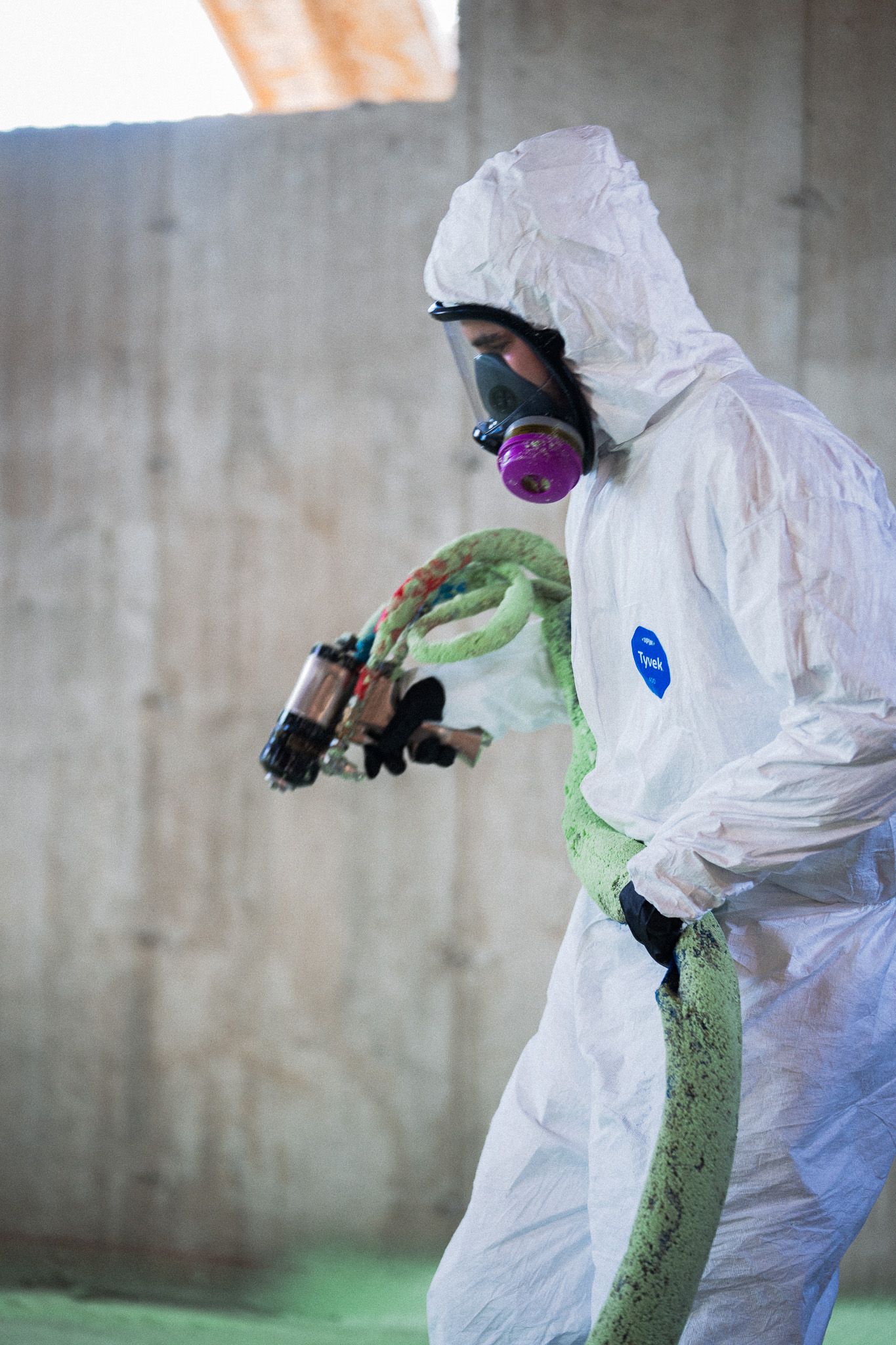 A man in a protective suit is spraying foam on a floor.
