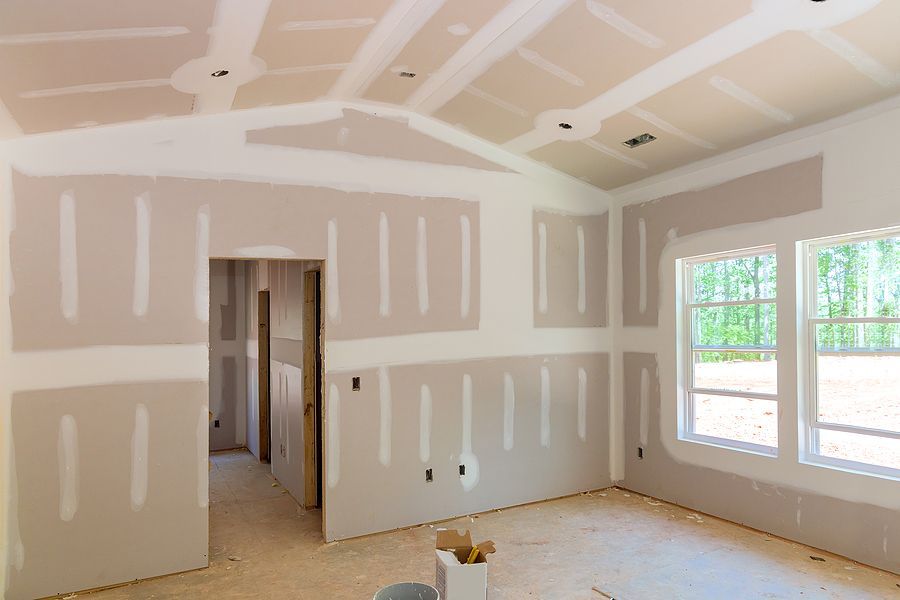 A room under construction with taped drywall on walls and a vaulted ceiling, featuring a window and an open doorway.