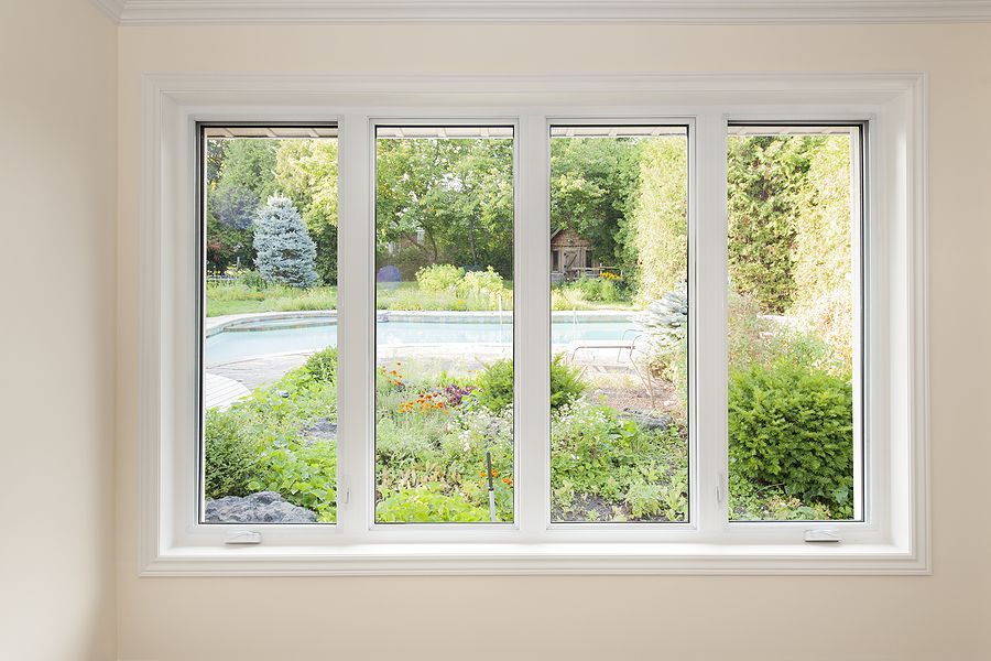 A white-framed, four-pane window looking out onto a lush backyard garden with a swimming pool and trees.