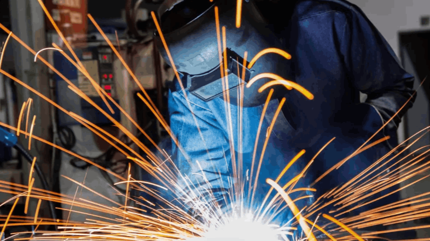 A man is welding a piece of metal in a factory.