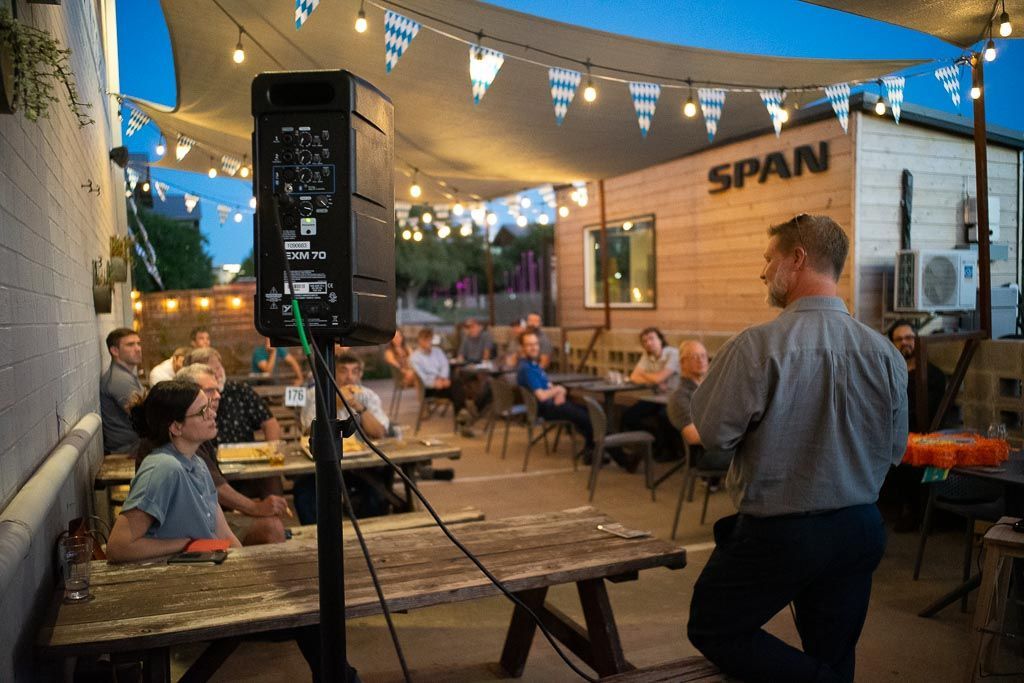 A man is giving a presentation to a group of people sitting at picnic tables.