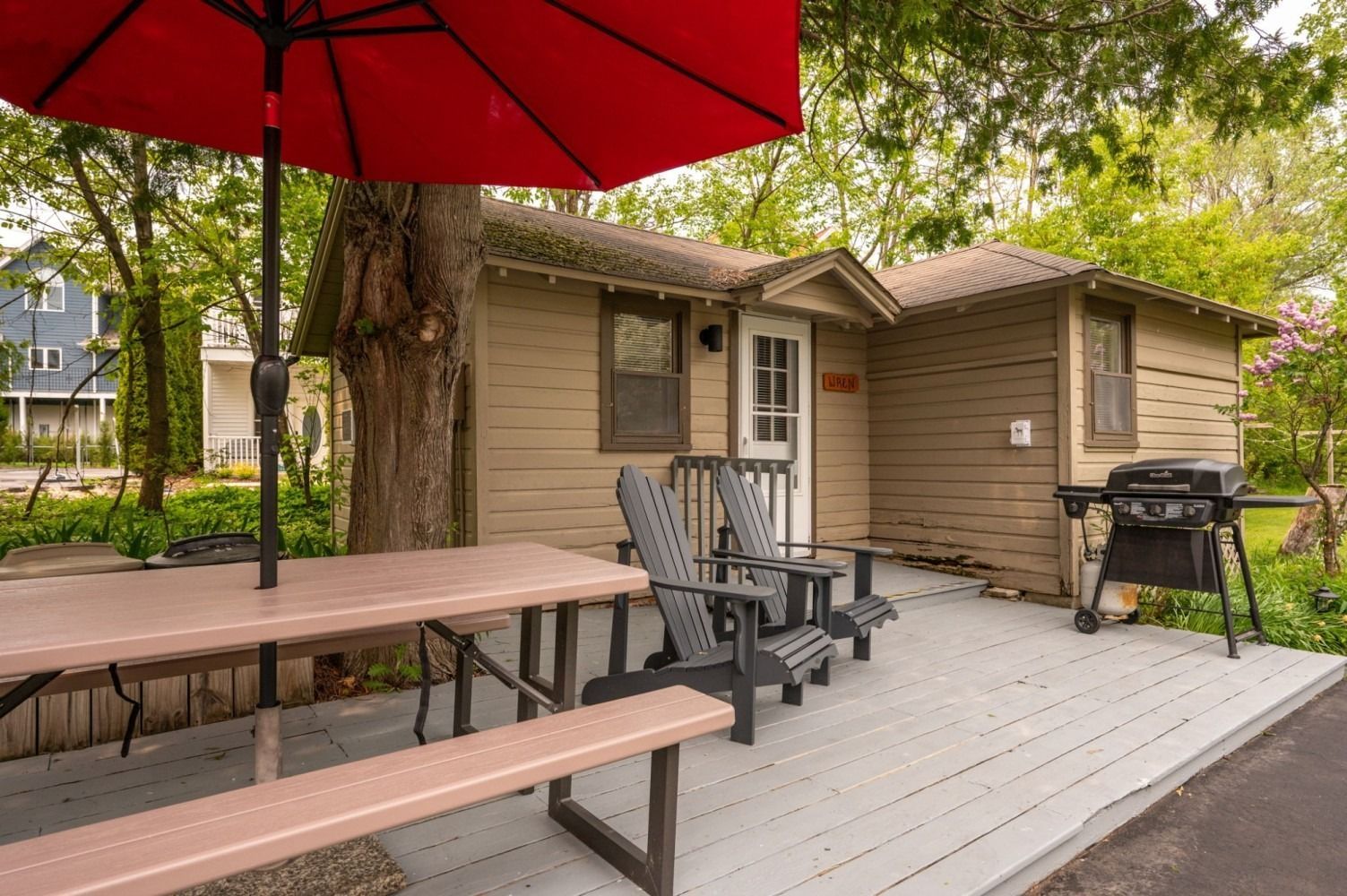 Small cabin with outdoor seating: picnic table, chairs, grill under a red umbrella.