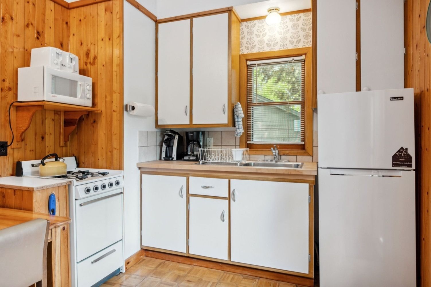 Small cabin kitchen with white appliances, wooden cabinets and walls.