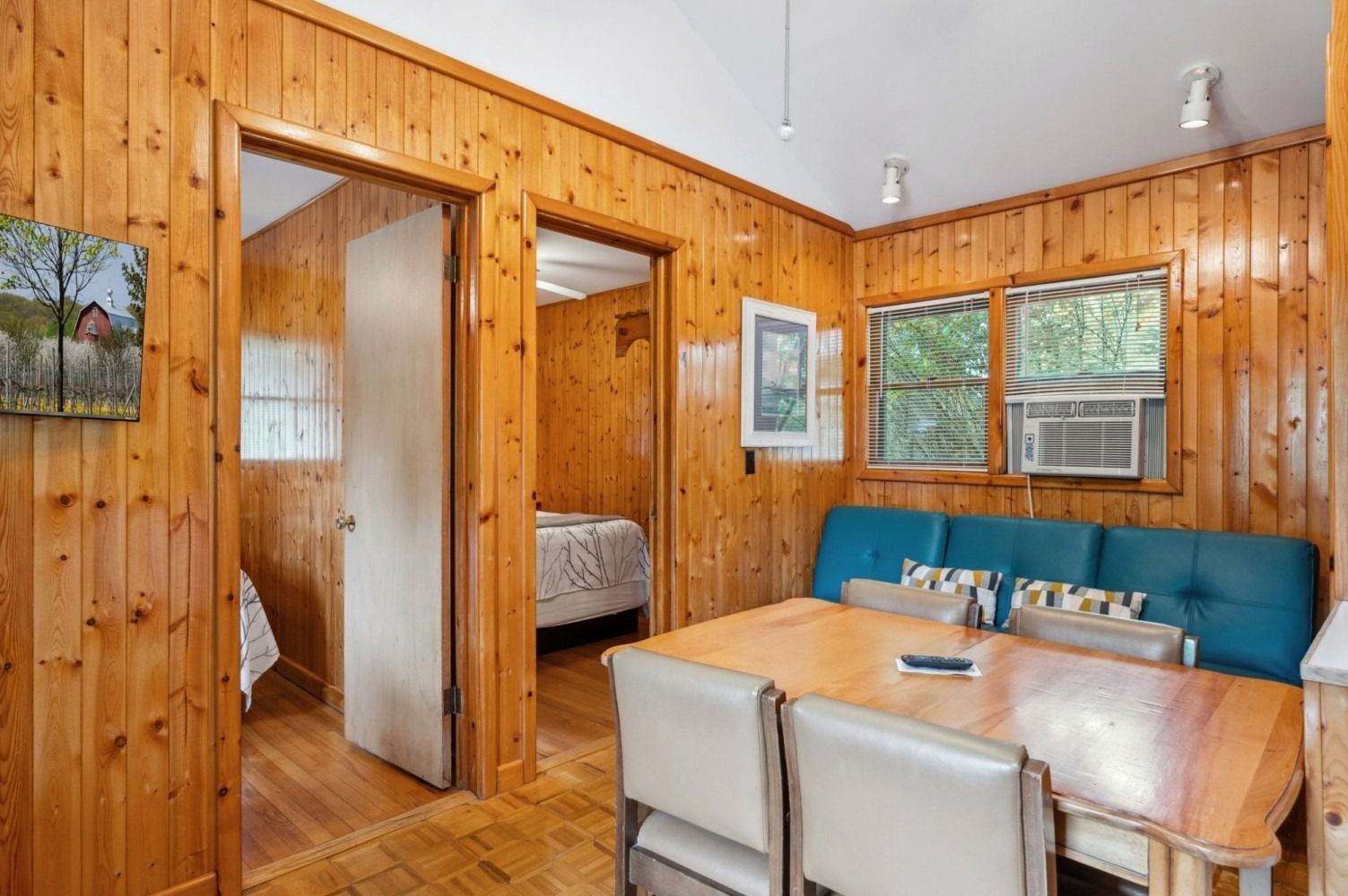 Interior of a small cabin with wood paneling. Dining table and sofa near a window. Two doorways lead to other rooms.