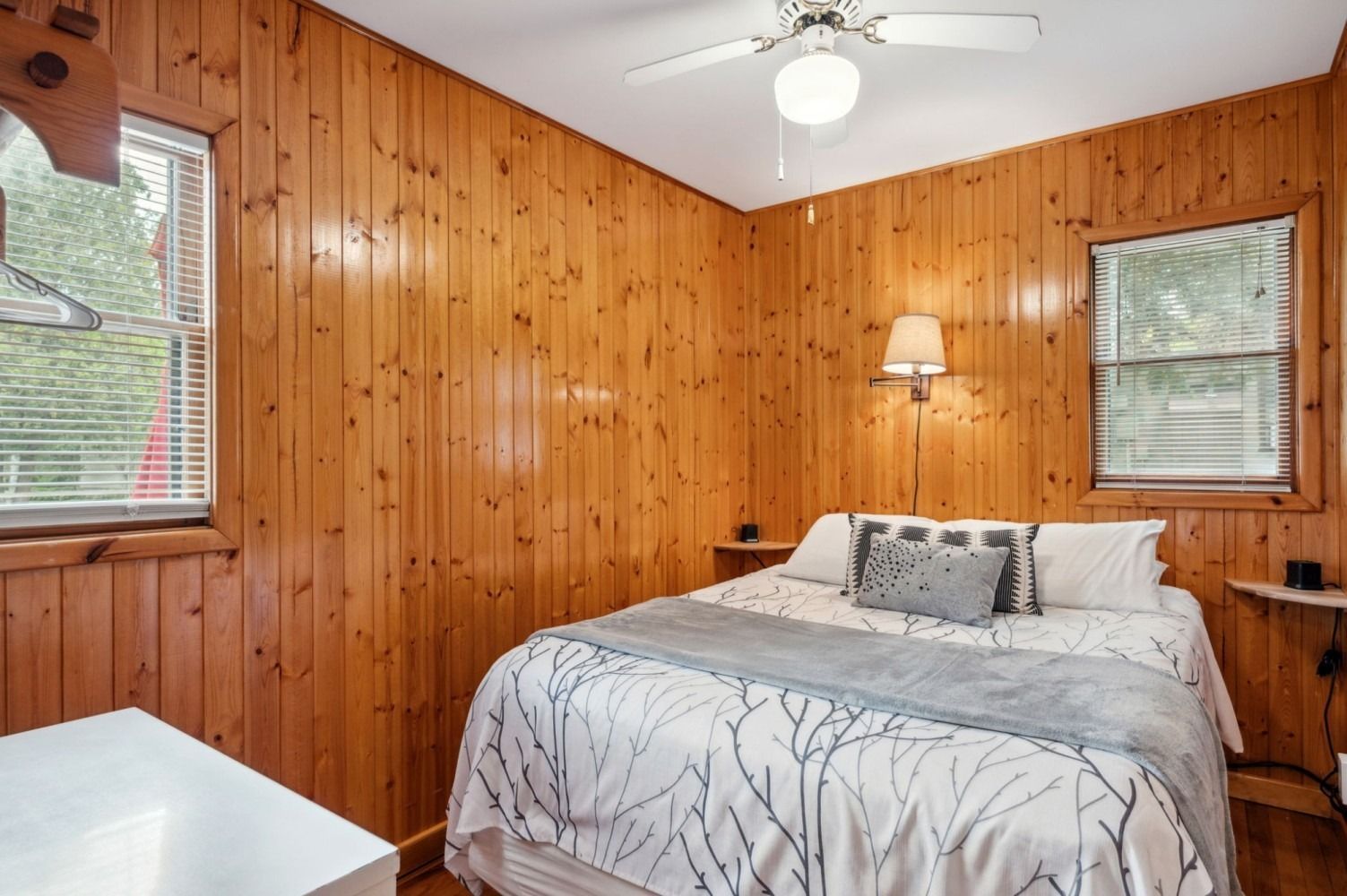 Bedroom with wood paneling, a bed with white bedding, and two windows.