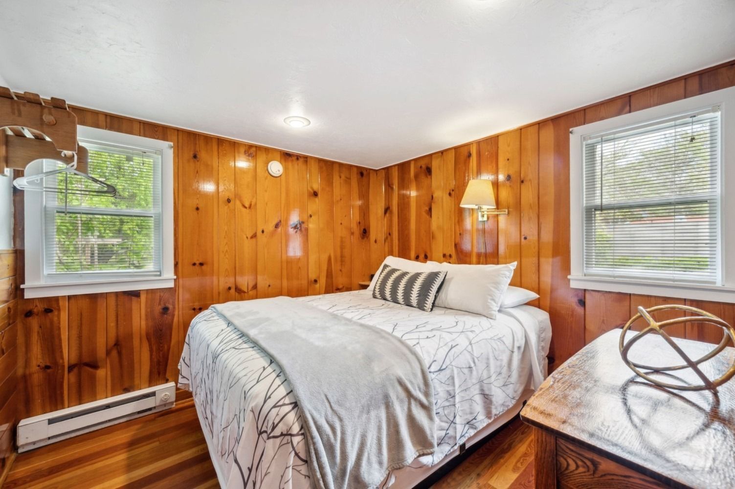 Bedroom with wood paneling, a bed with white bedding, and two windows.