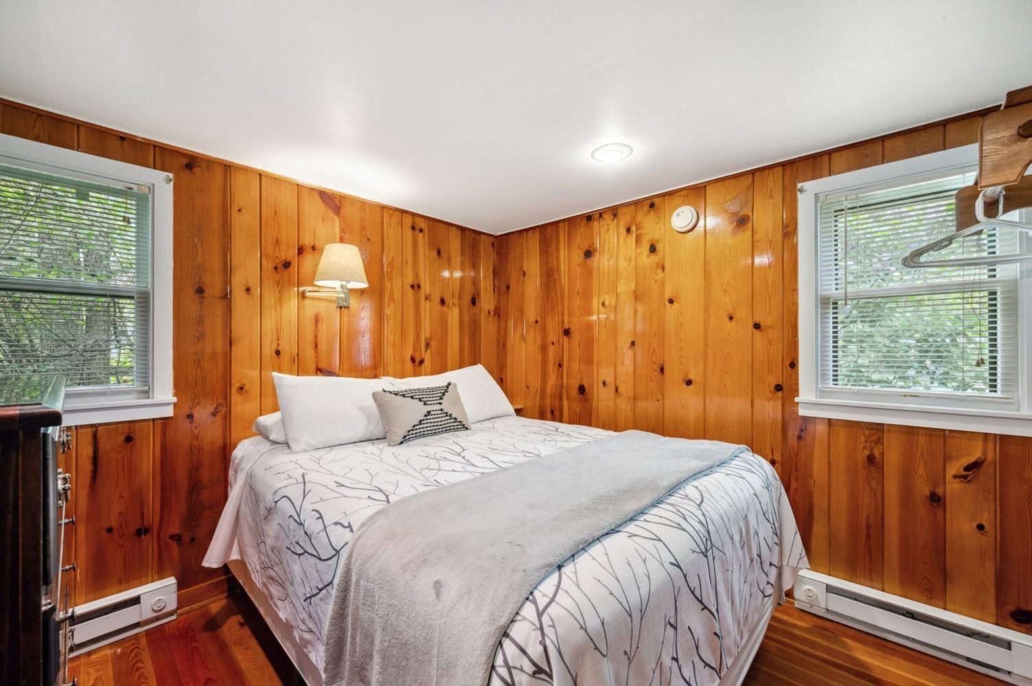 Bedroom with wood-paneled walls, bed with white bedding, and two windows.