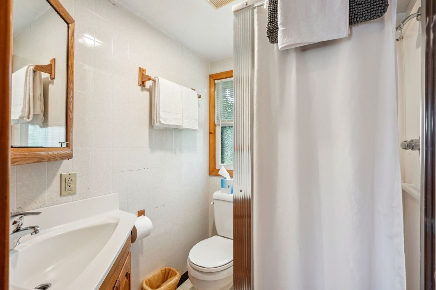 Bathroom with white tiles, sink, toilet, shower curtain, towels, and a window.