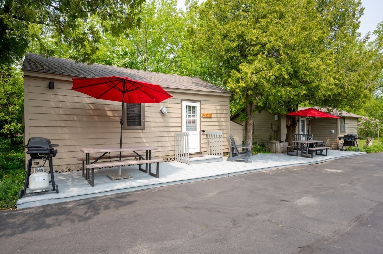 Cabin exterior with red umbrella, picnic table, grill, and trees.