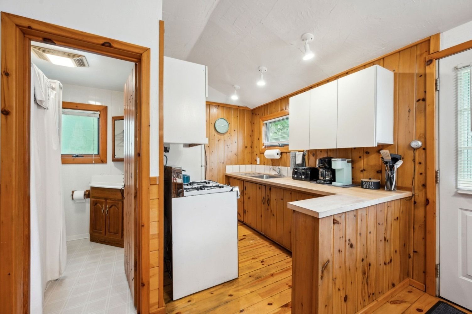 Small kitchen with wood paneling, white appliances, and a bathroom doorway visible.