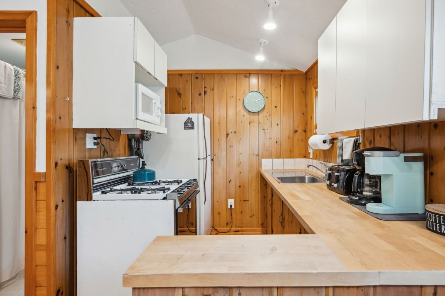 Small kitchen with white cabinets, wood paneling, and a light blue coffee maker.