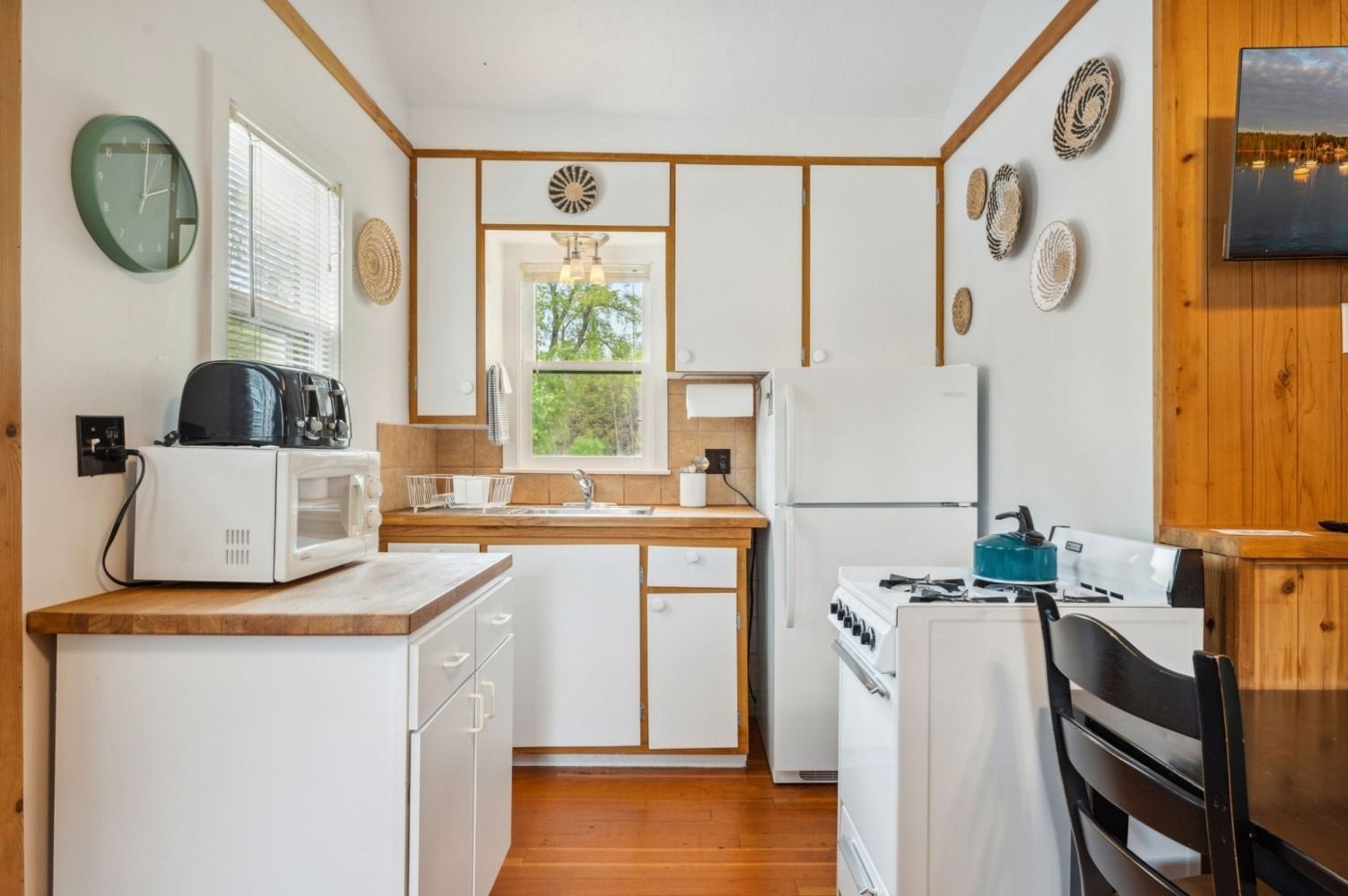 Small kitchen with white cabinets, appliances, and wood trim; window, plates on wall.