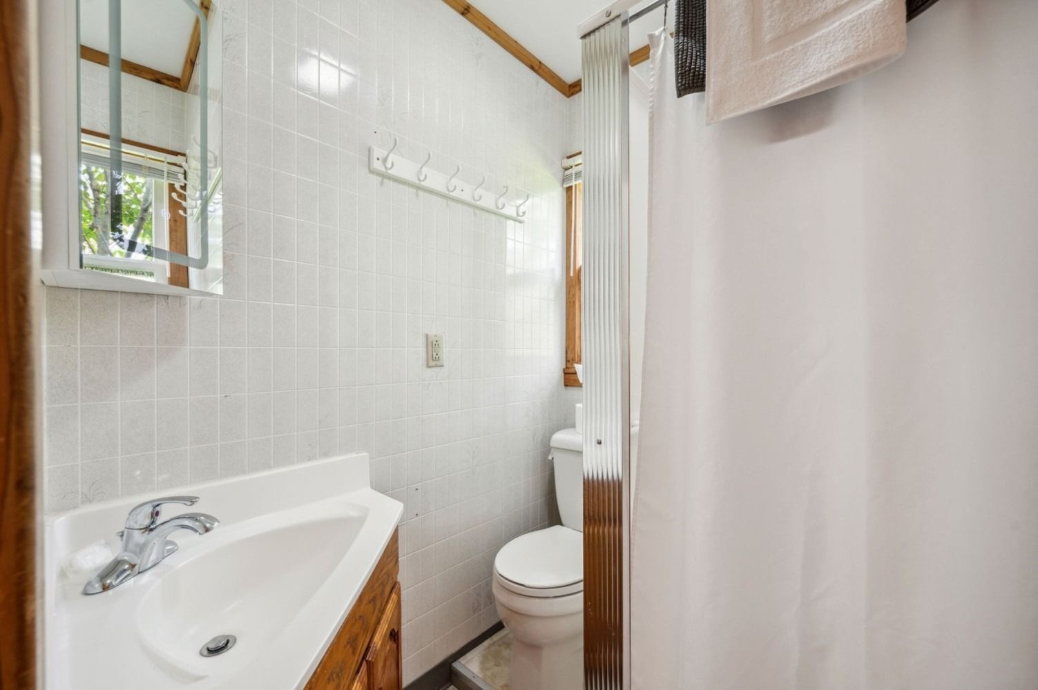 Small bathroom with white tiled walls, sink, toilet, and shower curtain.