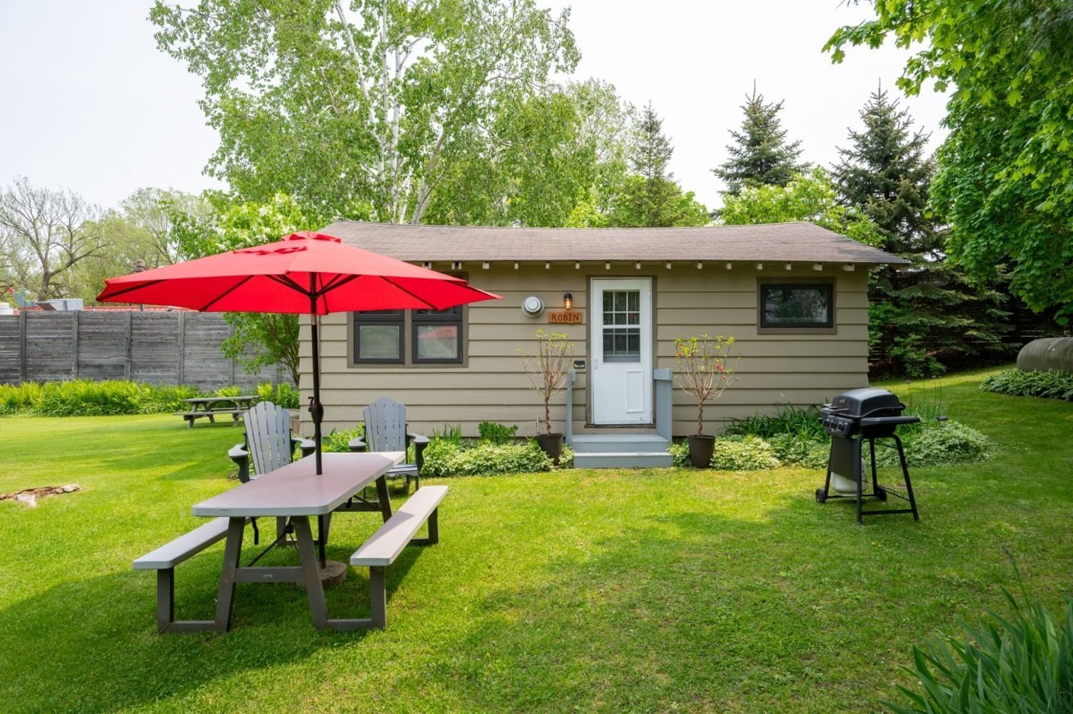 Cottage with red umbrella, picnic table, grill, and lush green lawn.