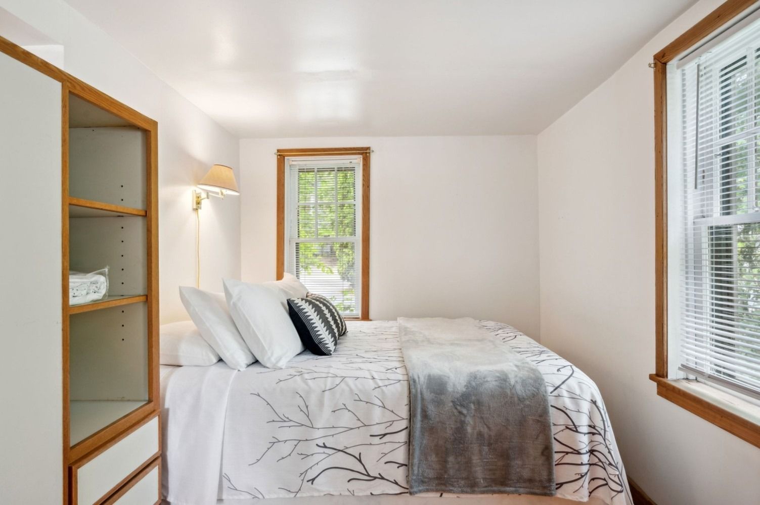 Bedroom with a white bed, floral bedding, window with blinds, and a white cabinet.