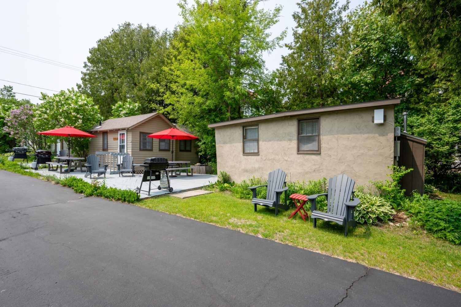 Two small buildings with outdoor seating and red umbrellas near trees.