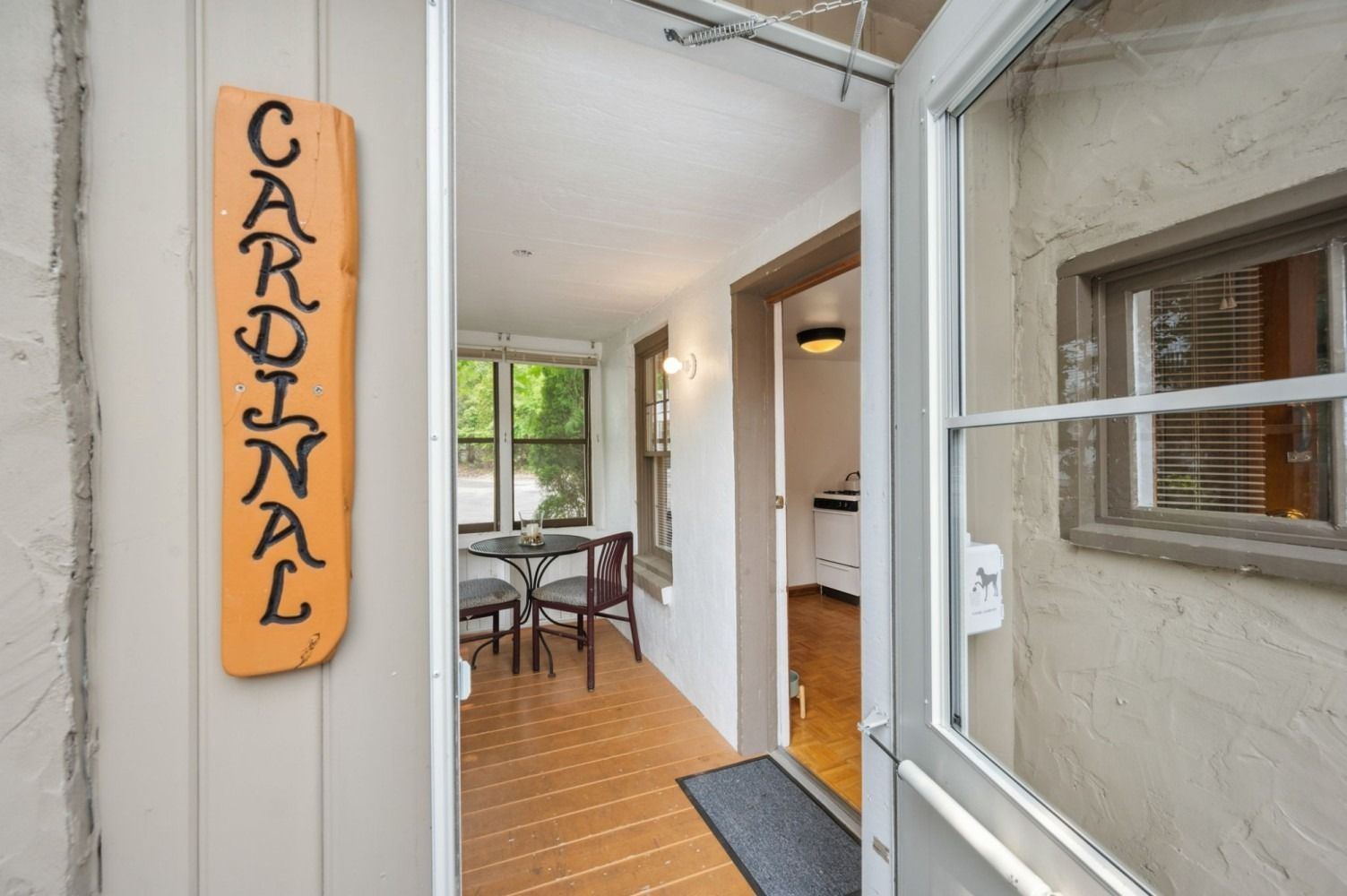 Open doorway into a small sunroom with a table and chairs, a sign that says 