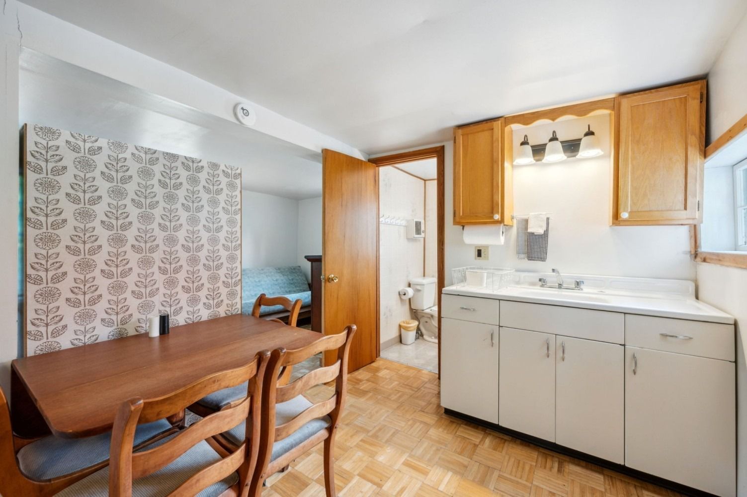 Small kitchen with wood table and cabinets, opening to a bedroom and bathroom.