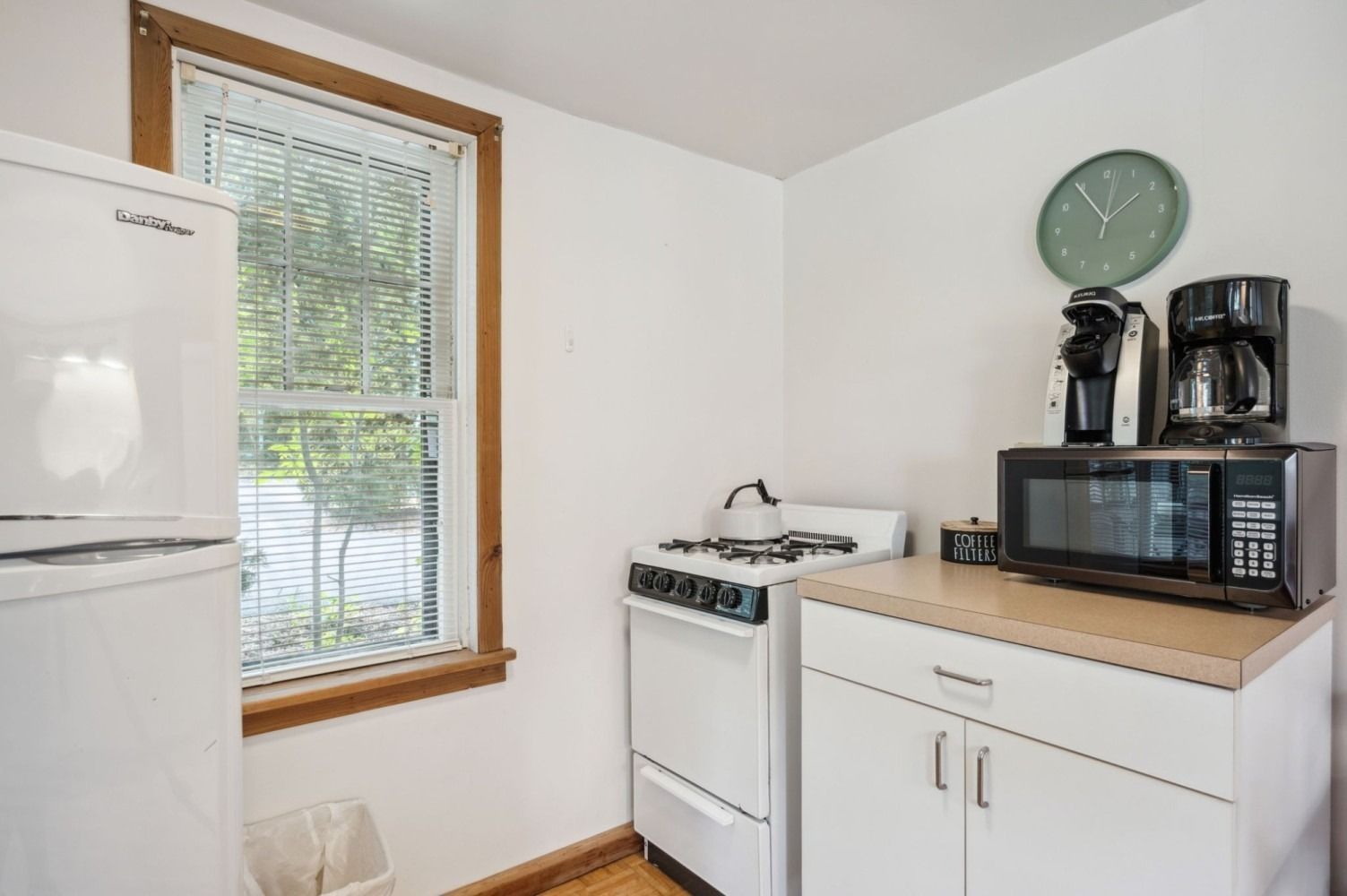 Small white kitchen with a refrigerator, stove, microwave, and coffee makers.