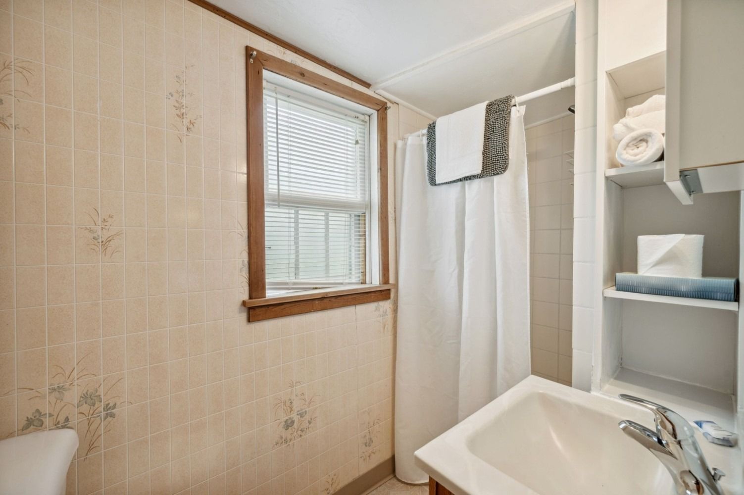 Small bathroom with floral wallpaper, window, shower curtain, and a sink.