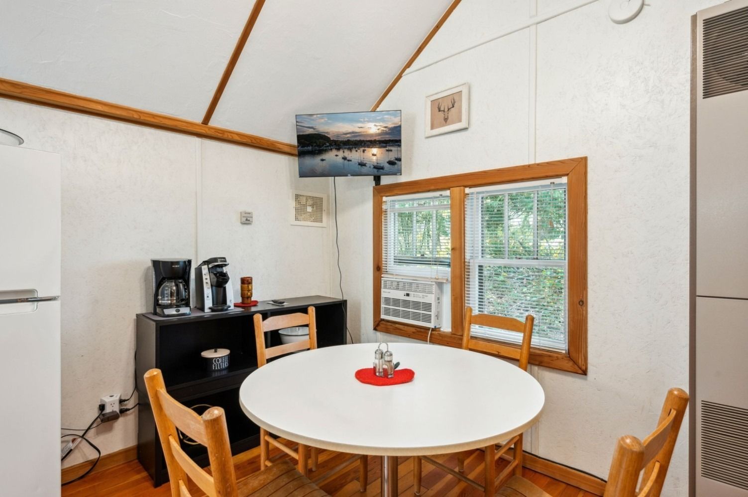 Small dining area with a round white table, wooden chairs, and a window with an AC unit.