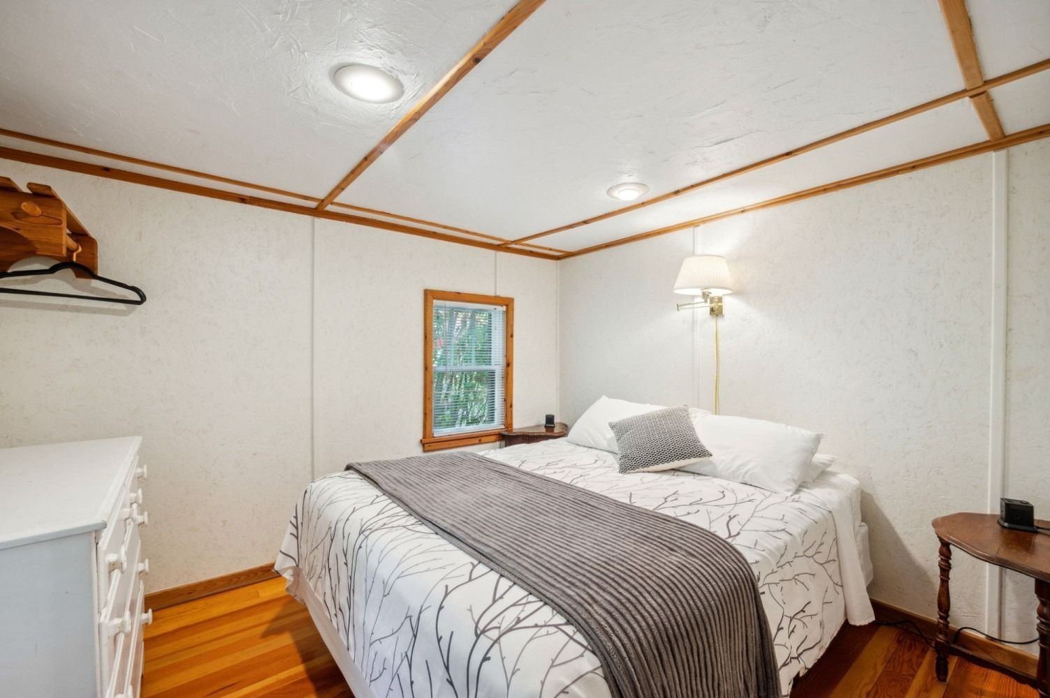 Bedroom with a double bed, white walls, wood trim, and a small window overlooking greenery.