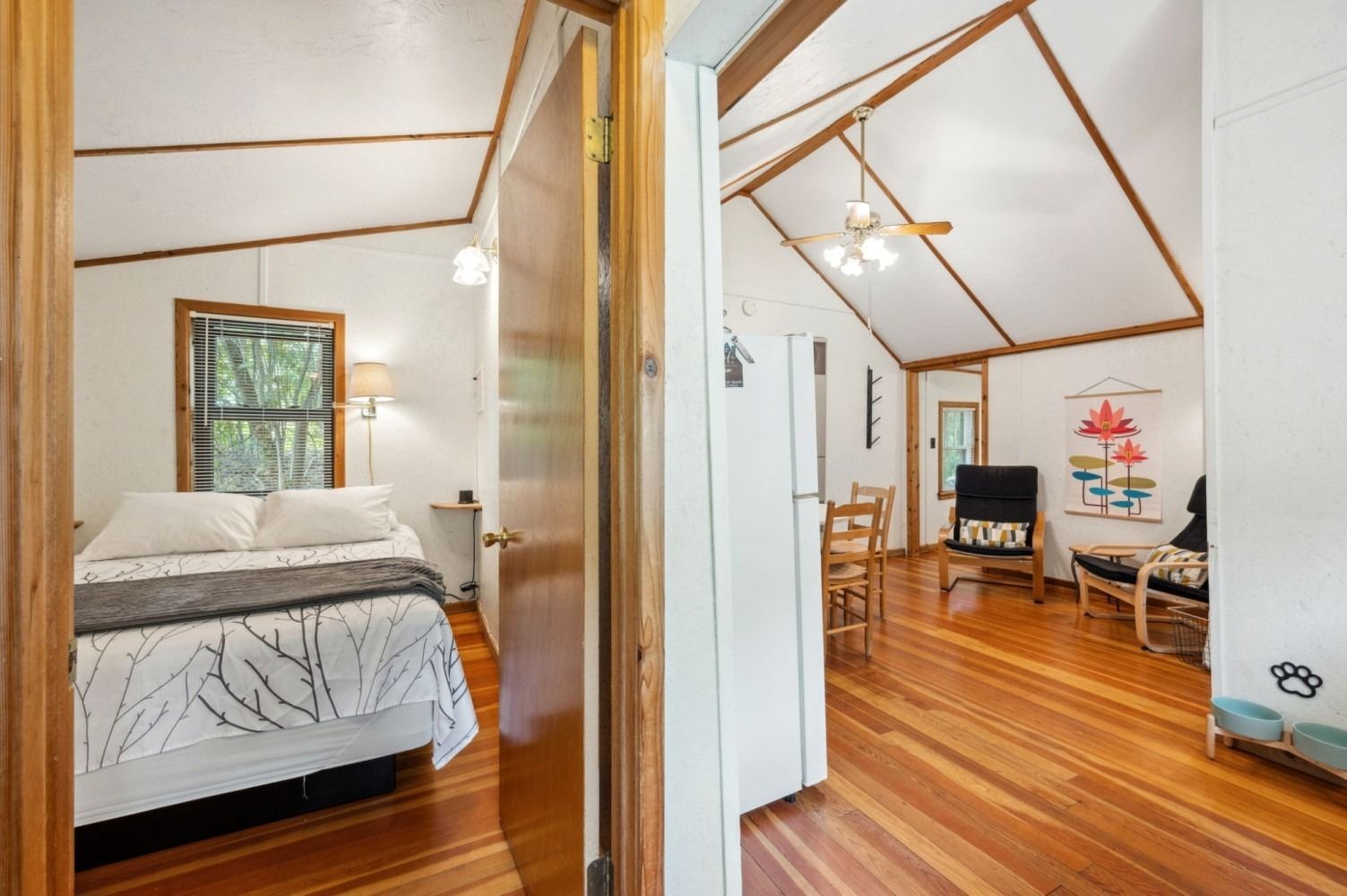 Interior view of a cabin with a bedroom and a living area, hardwood floors, and a vaulted ceiling.