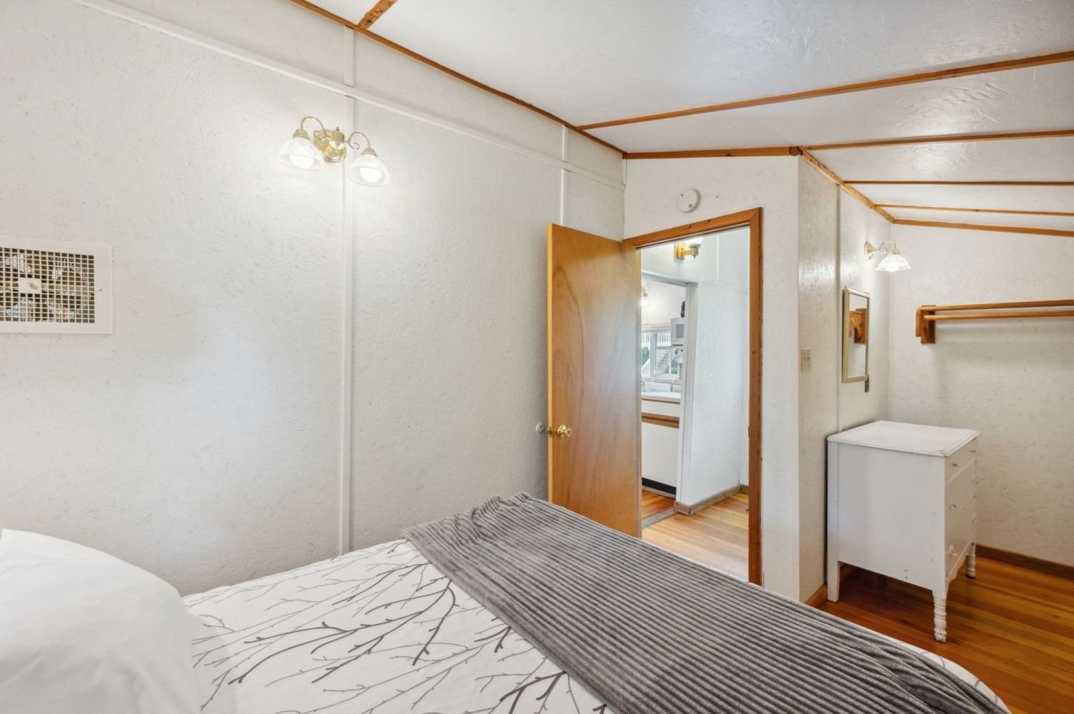 Bedroom interior with bed, open door to bathroom, white walls, wood trim.