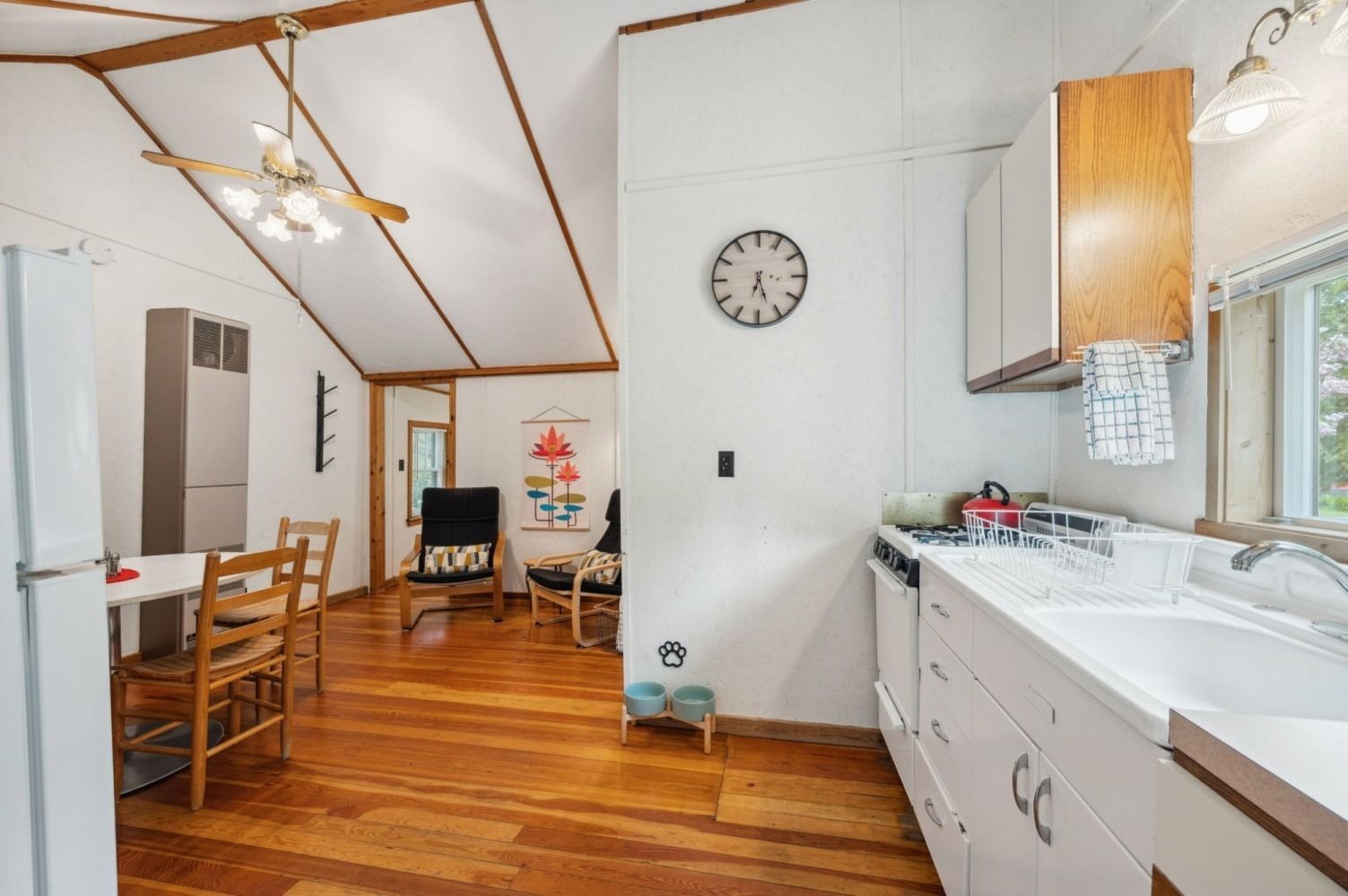 Kitchen and dining area with white cabinets, wooden floor, and a view into the living room.