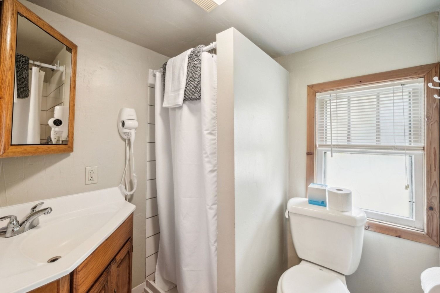 Small bathroom with a toilet, shower, vanity, and window.