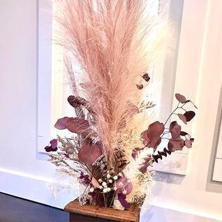 Floral arrangement with large pink pampas grass and burgundy dried flowers in a wooden base.