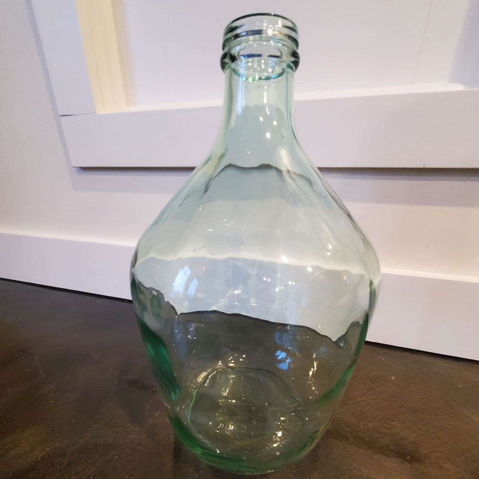 Large, light green glass bottle with a wide base and narrow neck, sitting indoors.