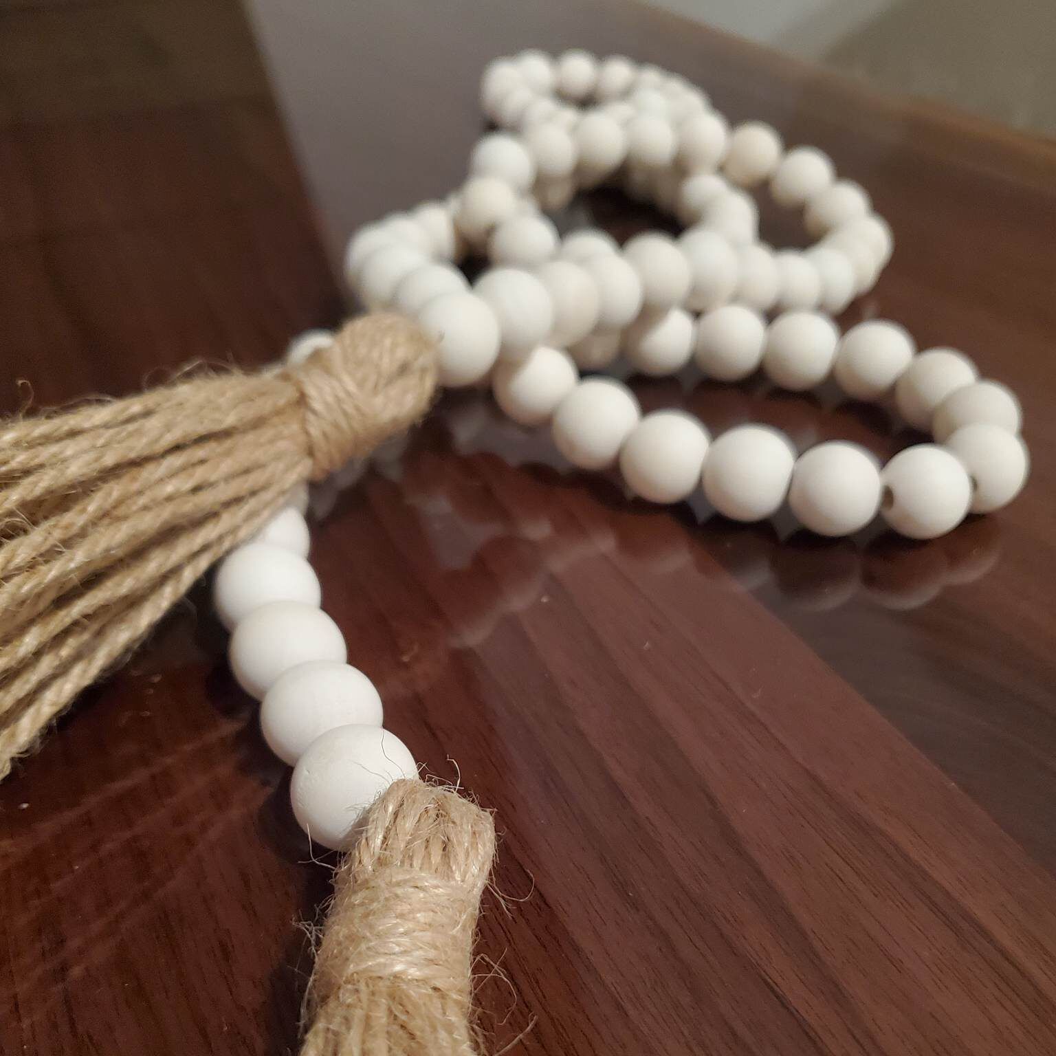 White beaded garland with jute tassels on a dark wood surface.