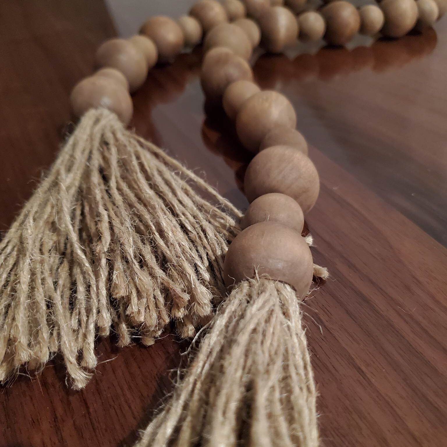 Wooden bead garland with jute tassels on a wood surface.