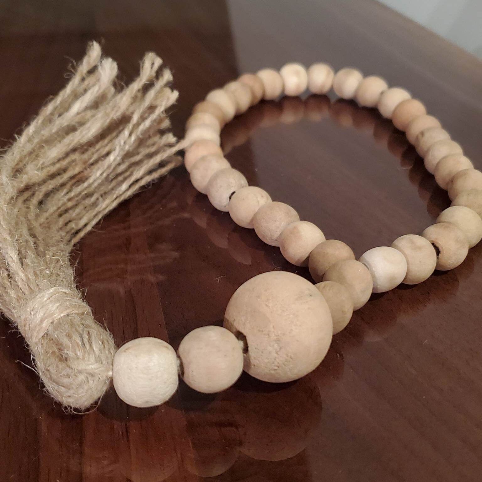 Wooden bead garland with a jute tassel resting on a dark, reflective surface.