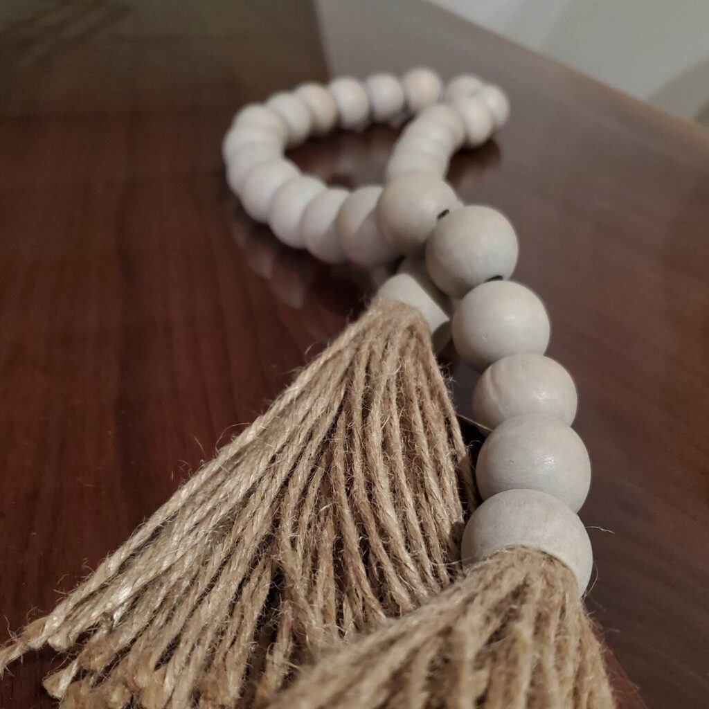 String of wooden beads with jute tassels, resting on a polished wooden surface.