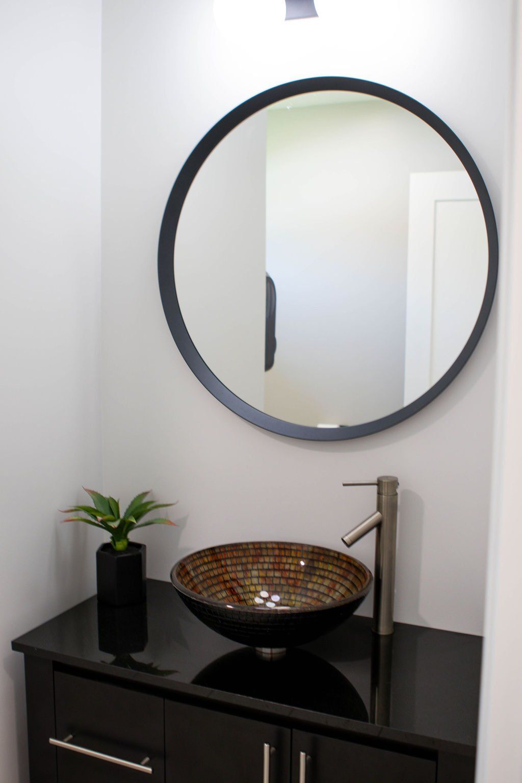 Modern bathroom with round mirror, mosaic sink bowl, and black cabinet.
