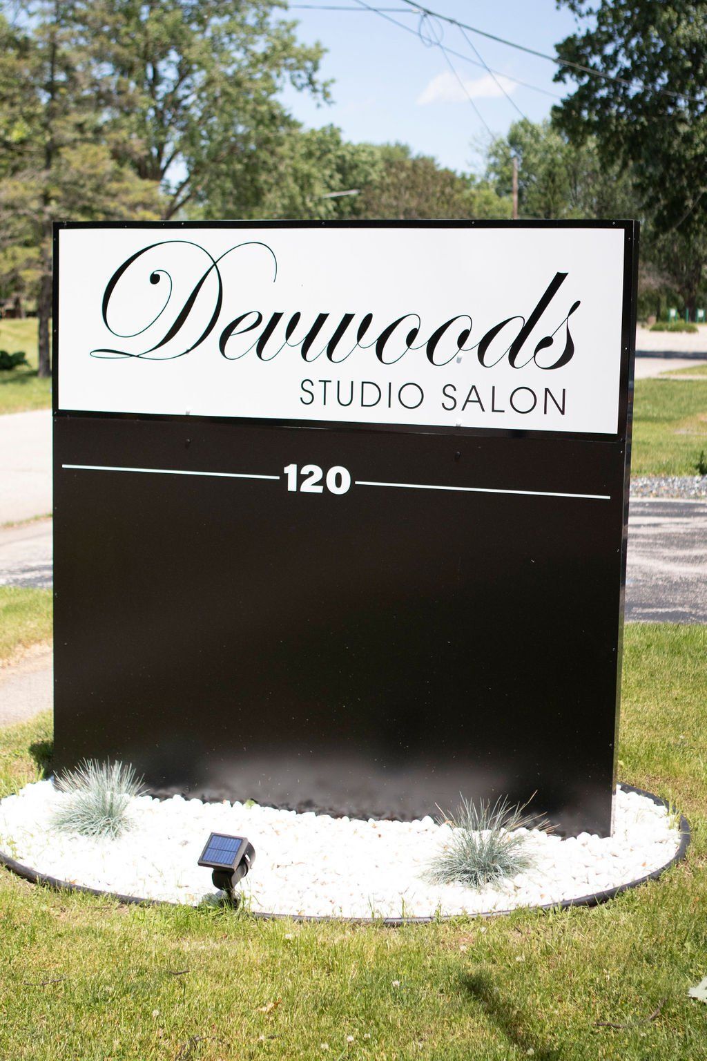Black and white sign for Devwoods Studio Salon, with address 120, set on a lawn with white stones.