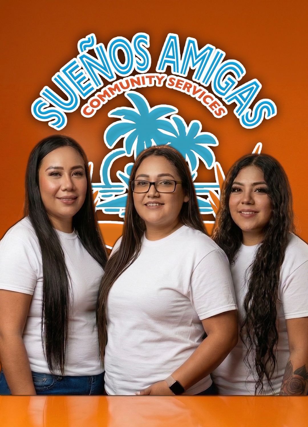 Three people in white shirts stand before an orange background with the Sueños Amigas Community Services logo above them.