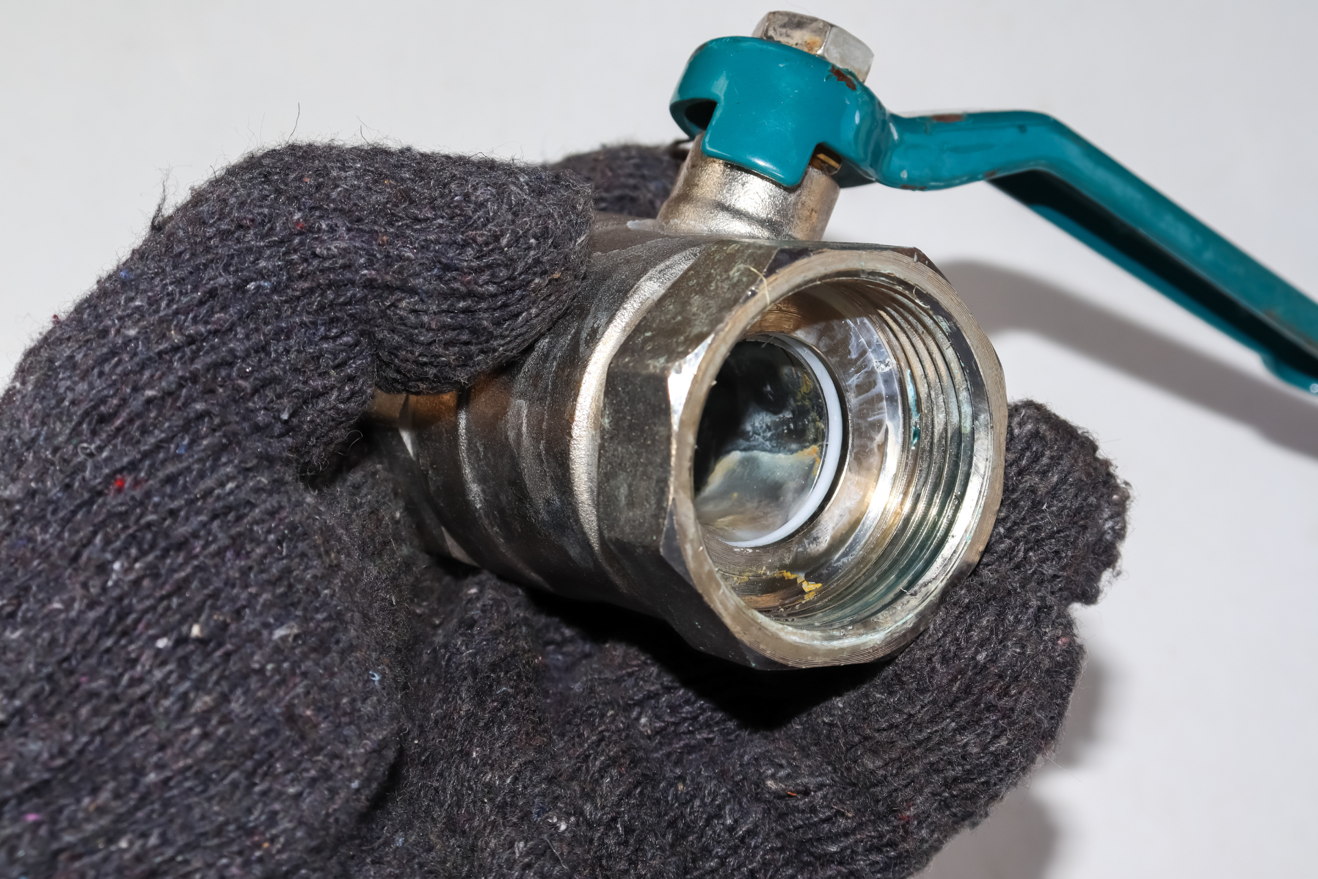 A person wearing a black glove is holding a valve with a blue handle.