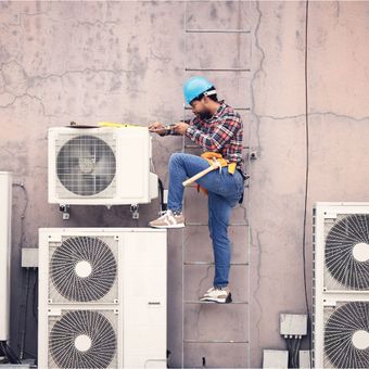 A man is standing on a ladder working on an air conditioner
