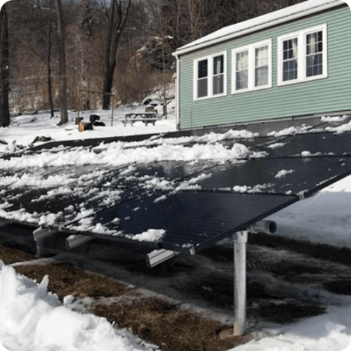A solar panel is sitting in the snow in front of a house.