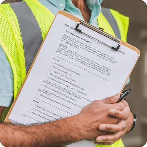Person in a safety vest holding a clipboard with a document and a pen, outdoors.