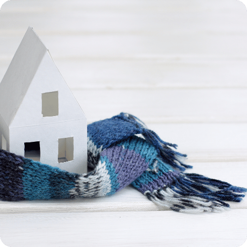 A white paper house wearing a blue and purple scarf, symbolizing warmth and winter preparedness.